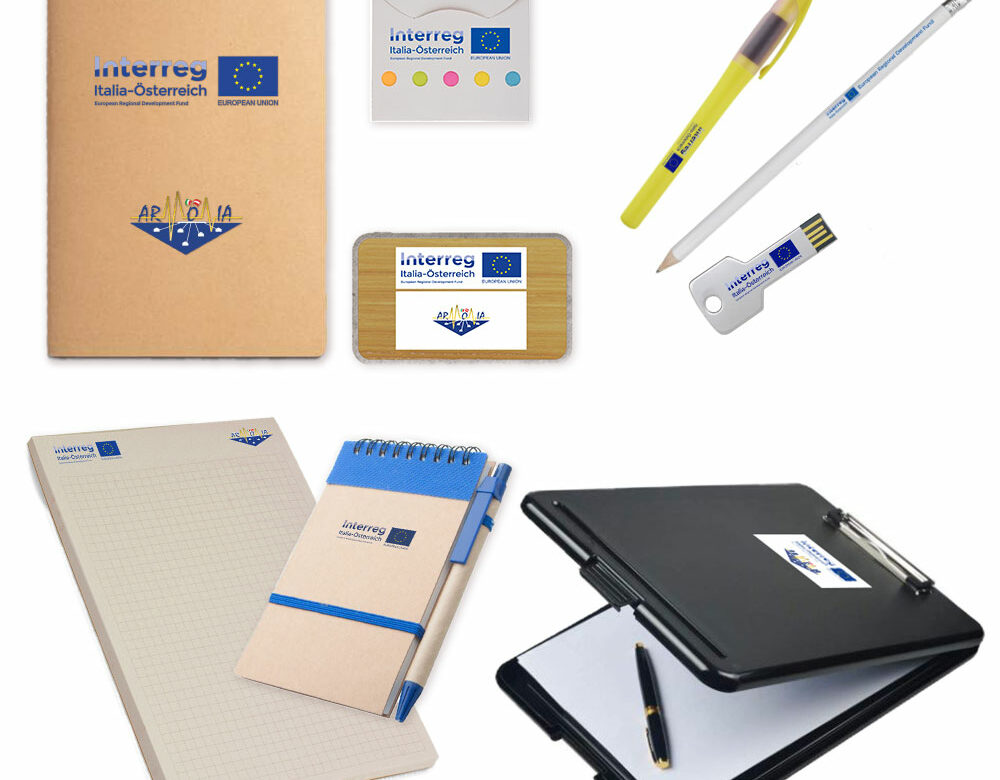 Gadget personalizzati per il progetto Interreg: quaderno ecologico, power bank, set post notes, evidenziatore, matita, chiavetta, block notes, tacquino ecologico e tavoletta porta blocco.